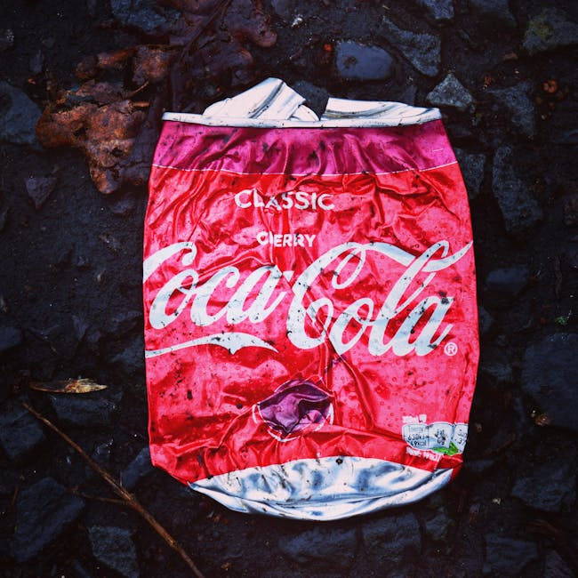 A collection of large, black plastic refuse bags filled with waste is positioned on the edge of a paved sidewalk, close to a curb. The bags are slightly crumpled, with some appearing to bulge at the s